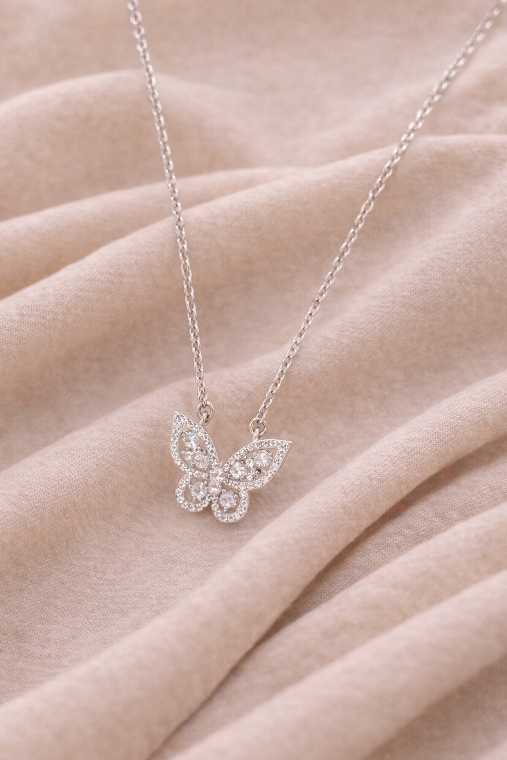 Silve butterfly pendant necklace with crystal accented wings displayed on a soft neutral fabric background