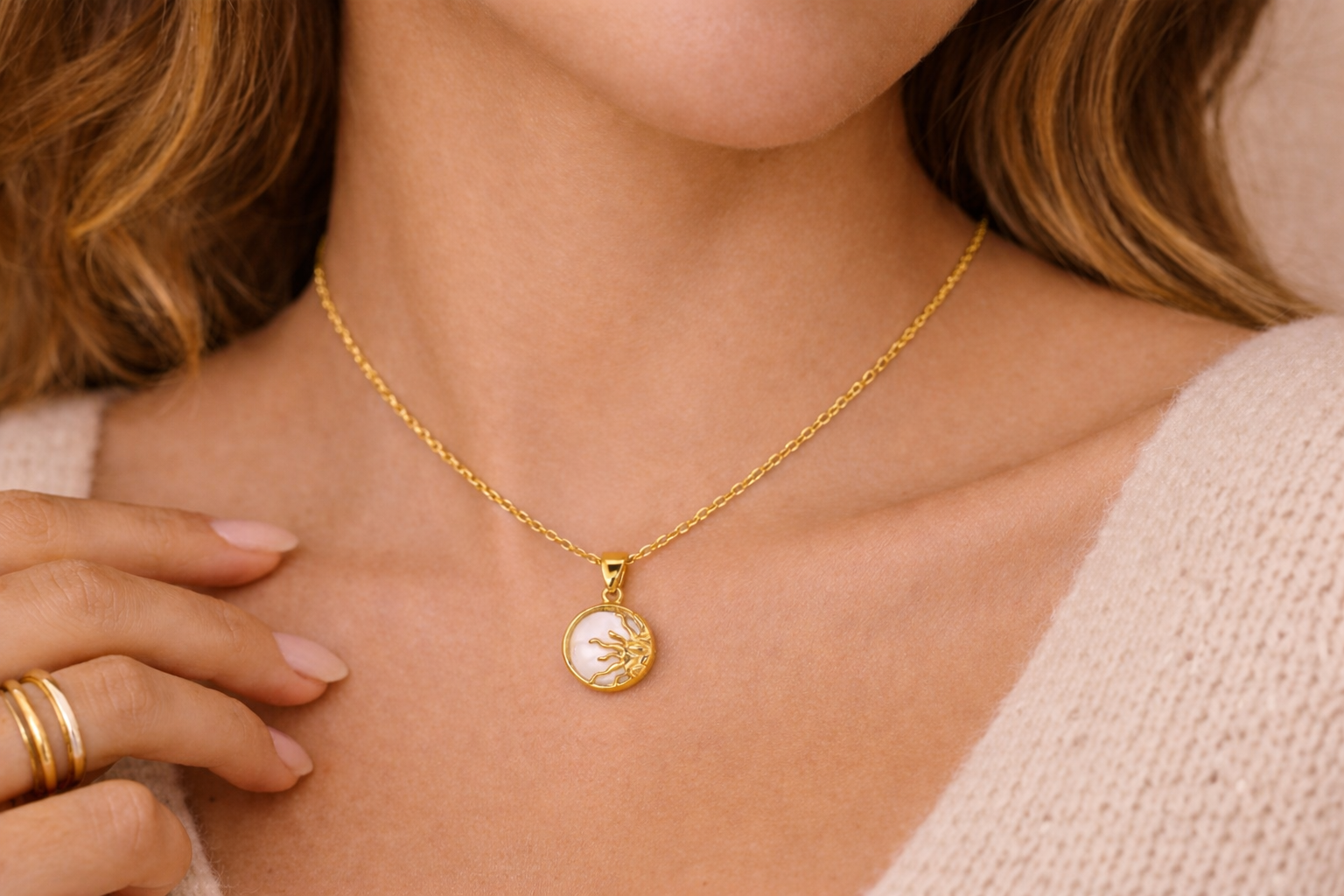 Gold sun pendant necklace with white center stone, worn on a model's neckline, featuring a delicate chain and small round charm