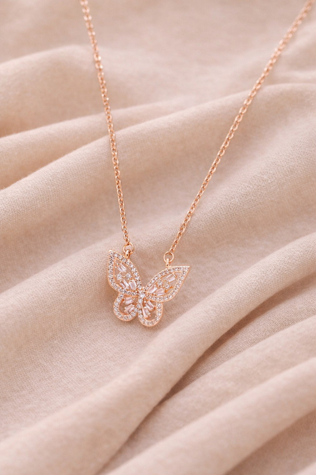 Rose gold butterfly pendant necklace with sparkling crystal accents displayed on soft neutral fabric