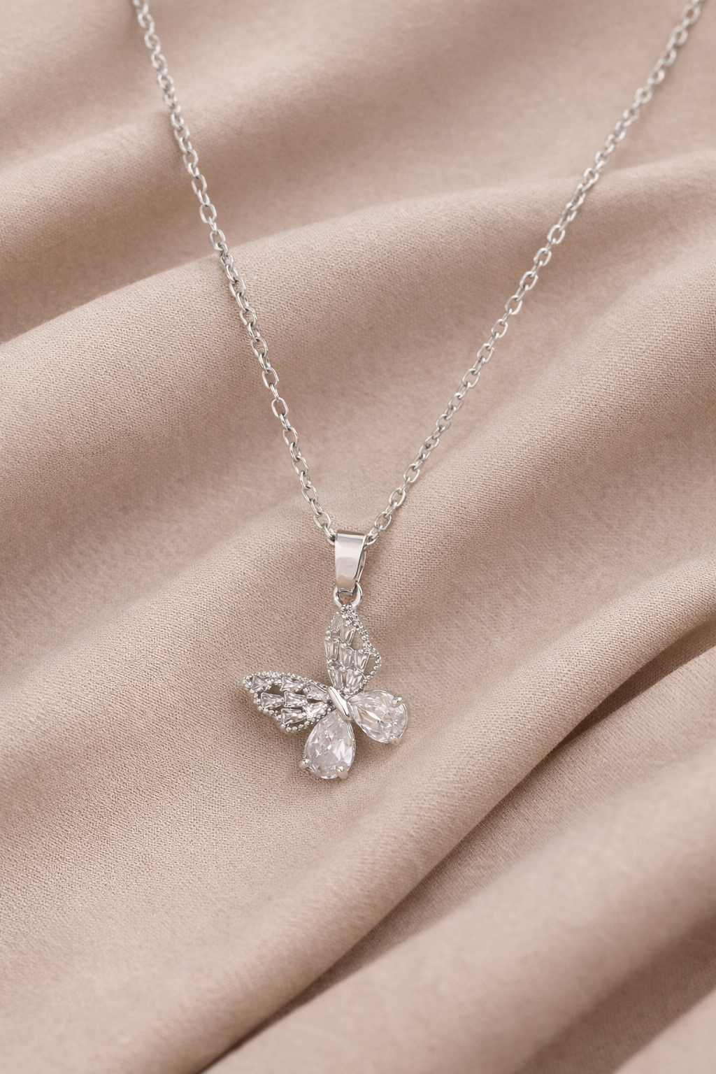 Silver butterfly pendant necklace with clear crystal details laid on beige neutral fabric for minimalist jewelry flat lay