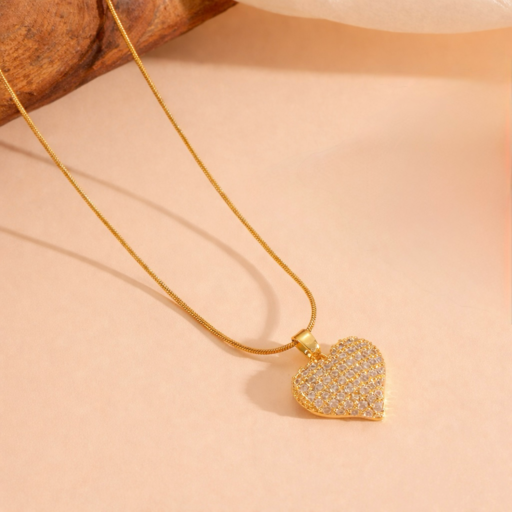 Gold heart pendant necklace with full pave crystals displayed on a warm beige surface