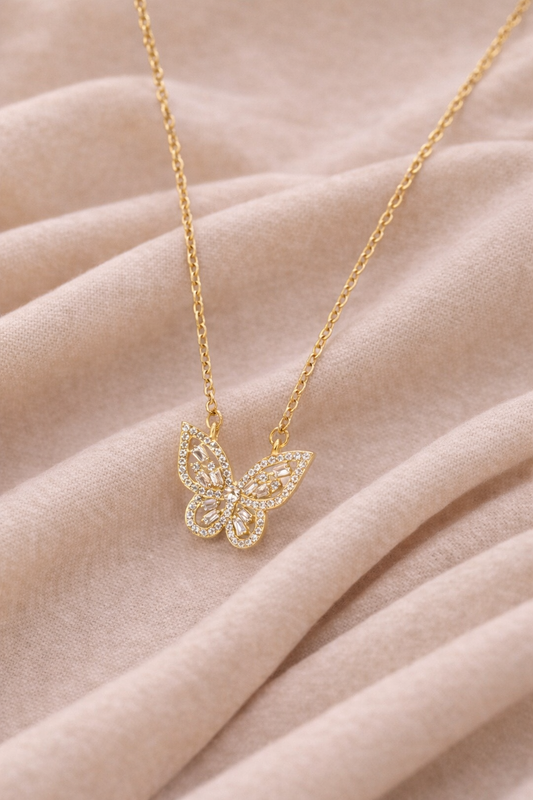 Gold butterfly pendant necklace with crystal detailed wings resting on a fabric with gentle folds