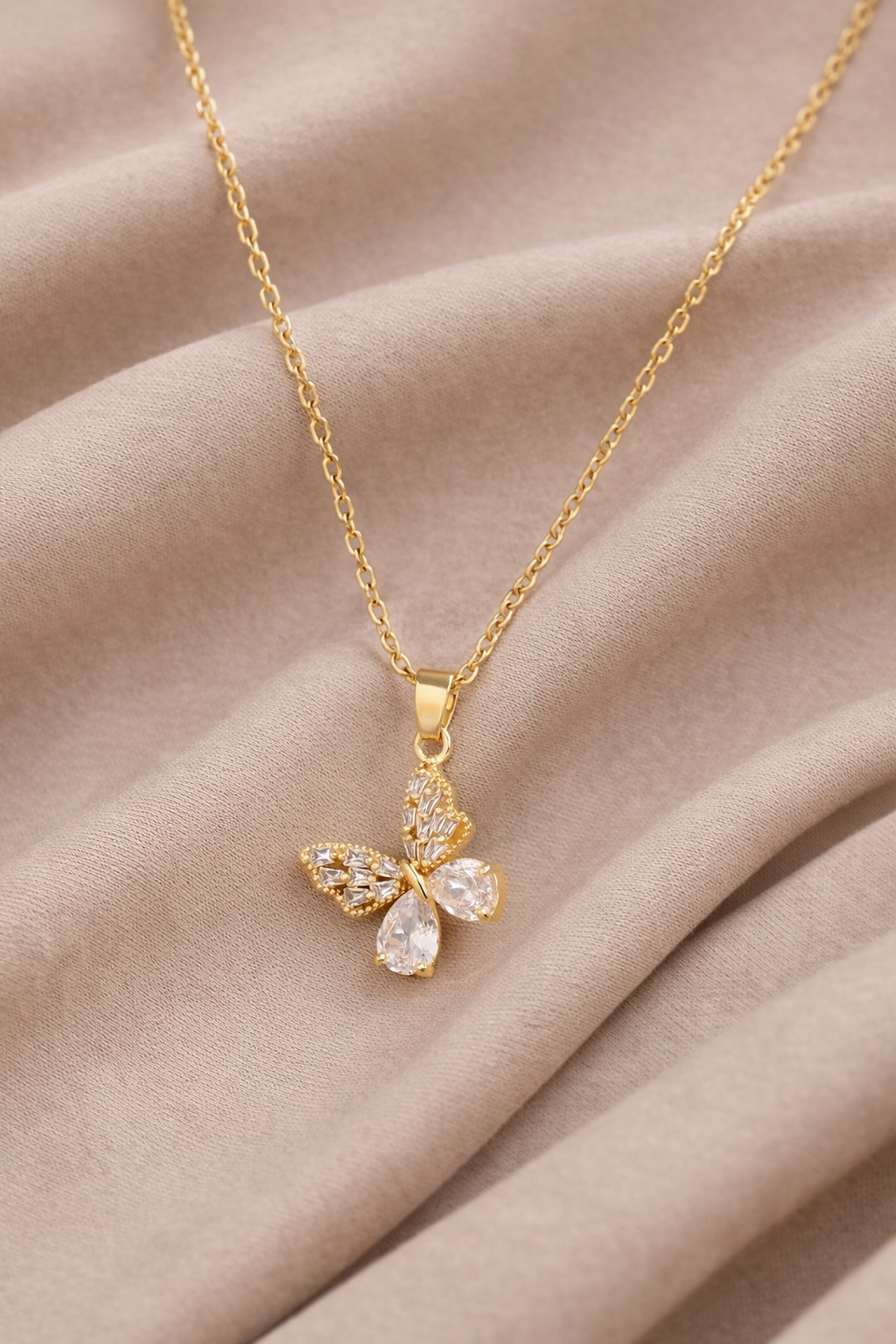 Gold Plated butterfly pendant necklace with sparkling crystal wings displayed on soft neutral fabric background