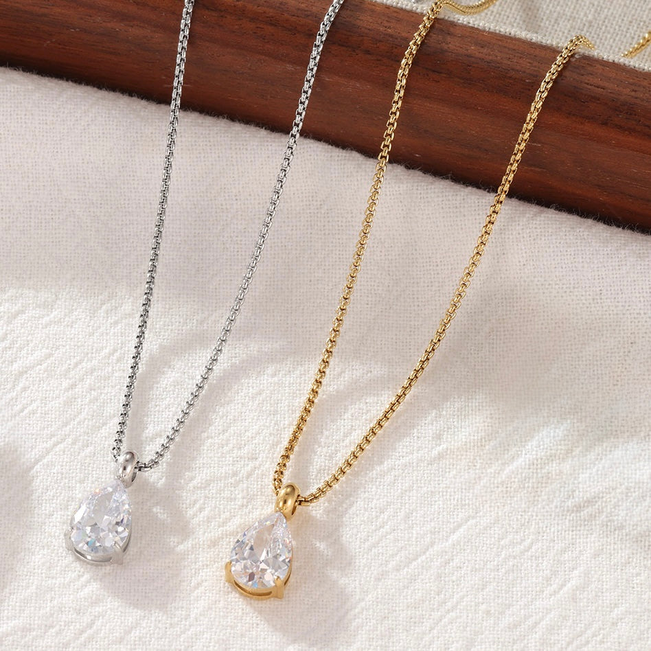 Gold and silver teardrop crystal pendant necklace on a neutral fabric background