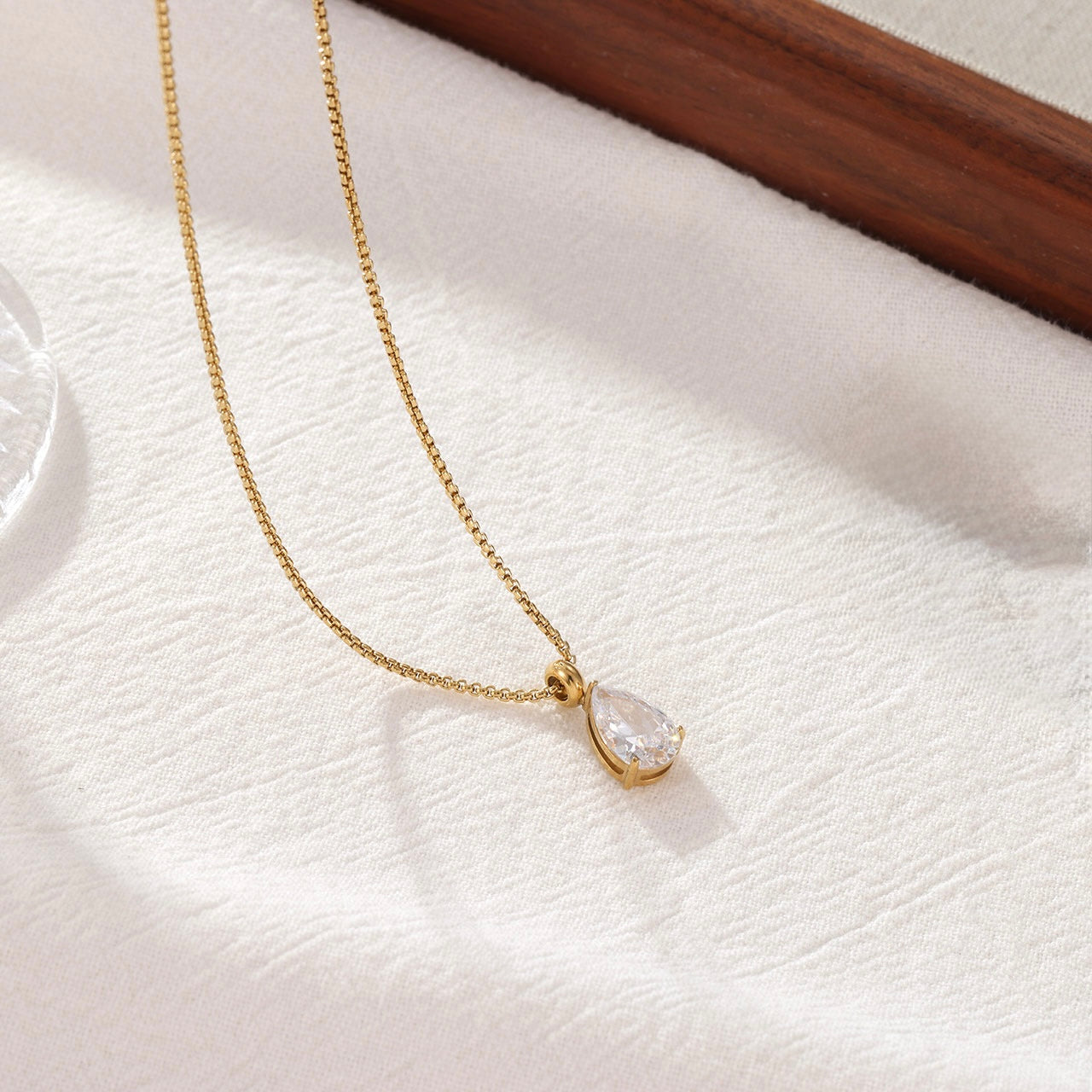 Lumi gold teardrop crystal pendant necklace on a white fabric background.