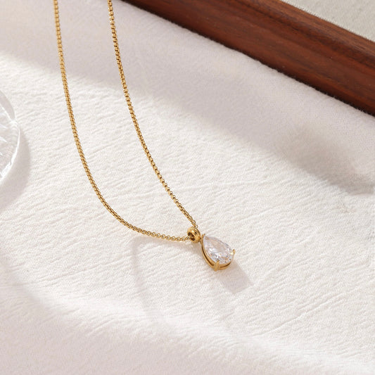 Lumi gold teardrop crystal pendant necklace on a white fabric background.