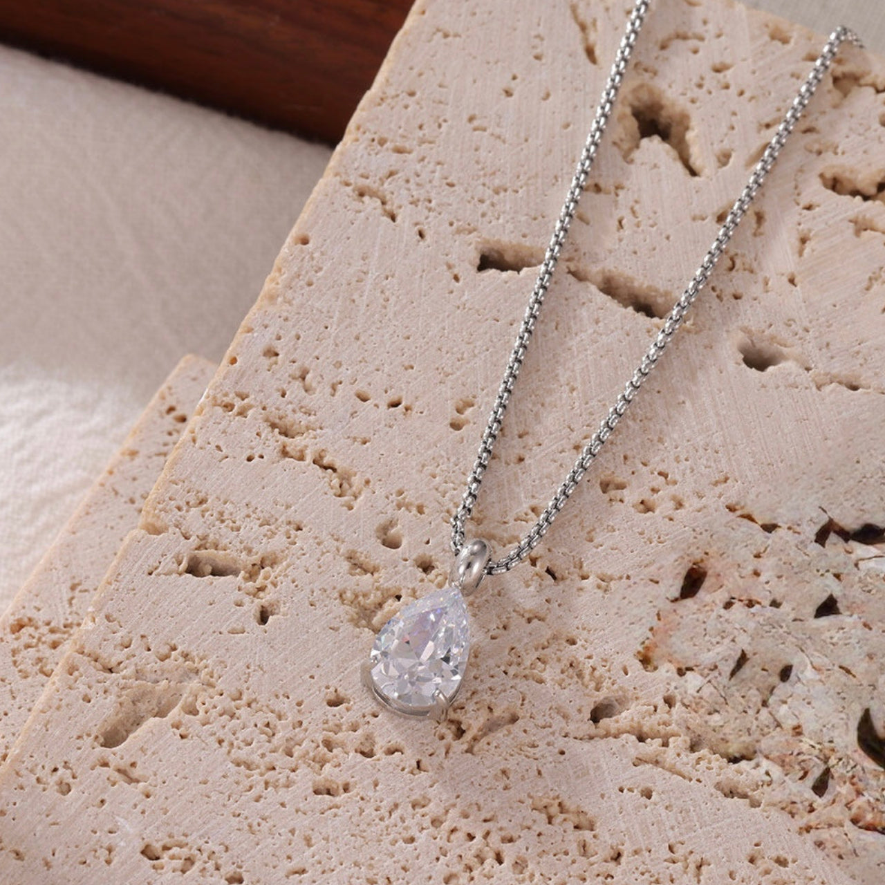 Lumi silver teardrop crystal pendant necklace on a textured stone surface